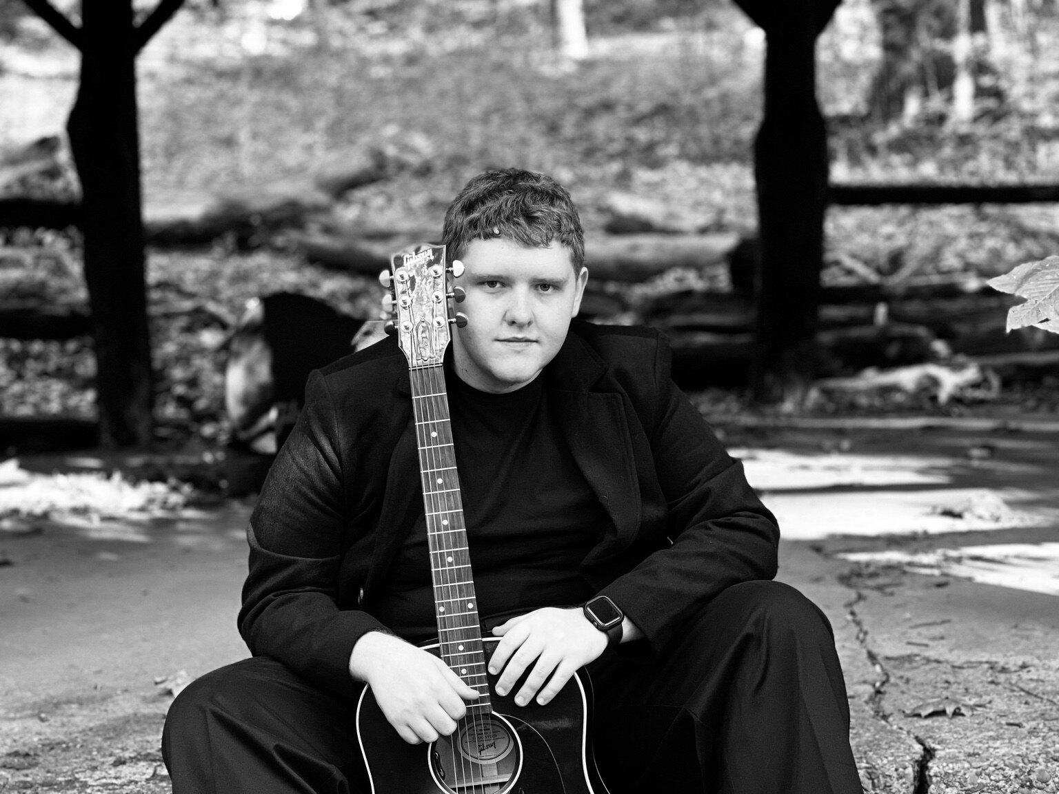 Black-and-white portrait of Jayce Walsh seated with an acoustic guitar